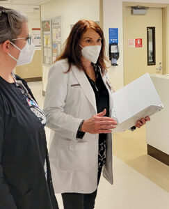 Nurse manager in white coat with folder talks to nursing staff.