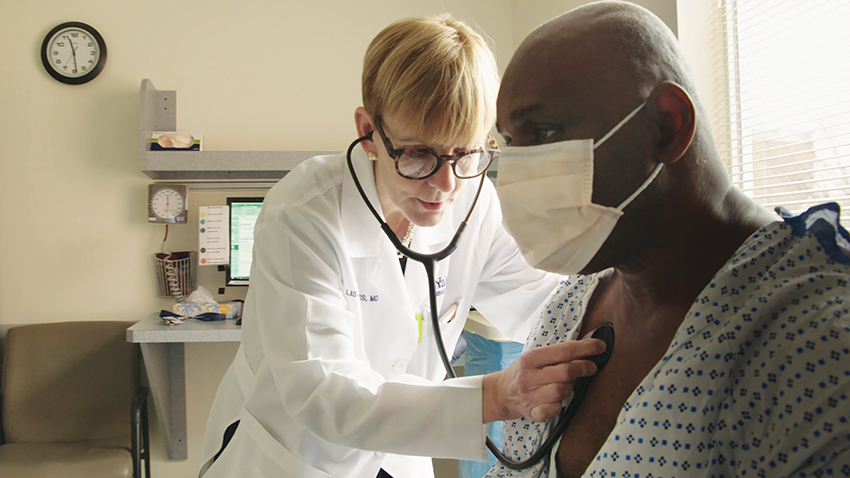 Female doctor in white coat listens to a patient's heart with a stethoscope.