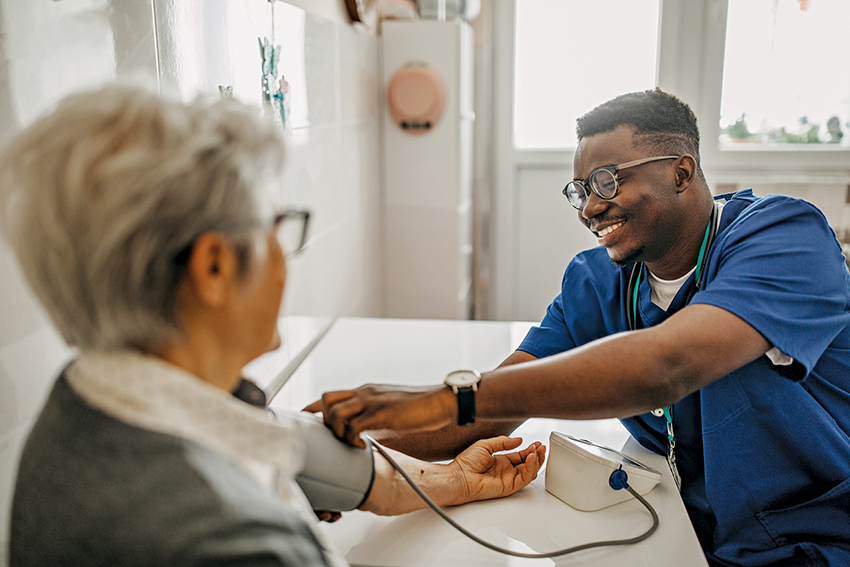 Smiling Black male nurse takes the blood pressure of an older white woman.