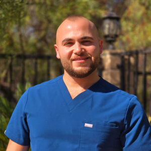 Male nurse in scrubs smiling and standing outside.