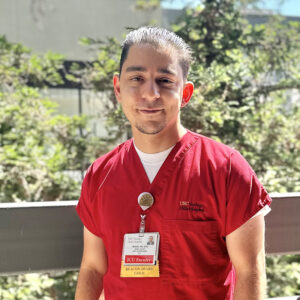 Male nurse in red scrubs standing outside.