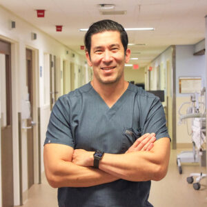 Male nurse in blue scrubs with arms folded, smiling