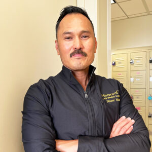 Male nurse with arms folded in a blue hoodie.